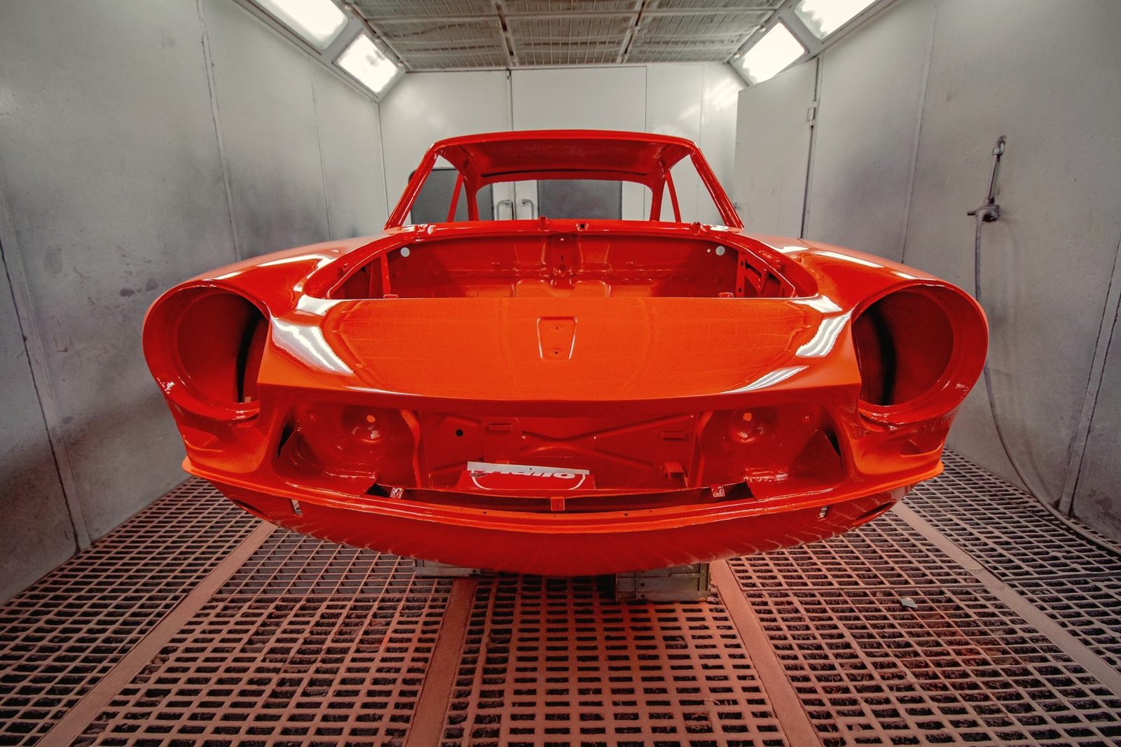 A freshly painted red car shell standing on the grated floor of a paint booth