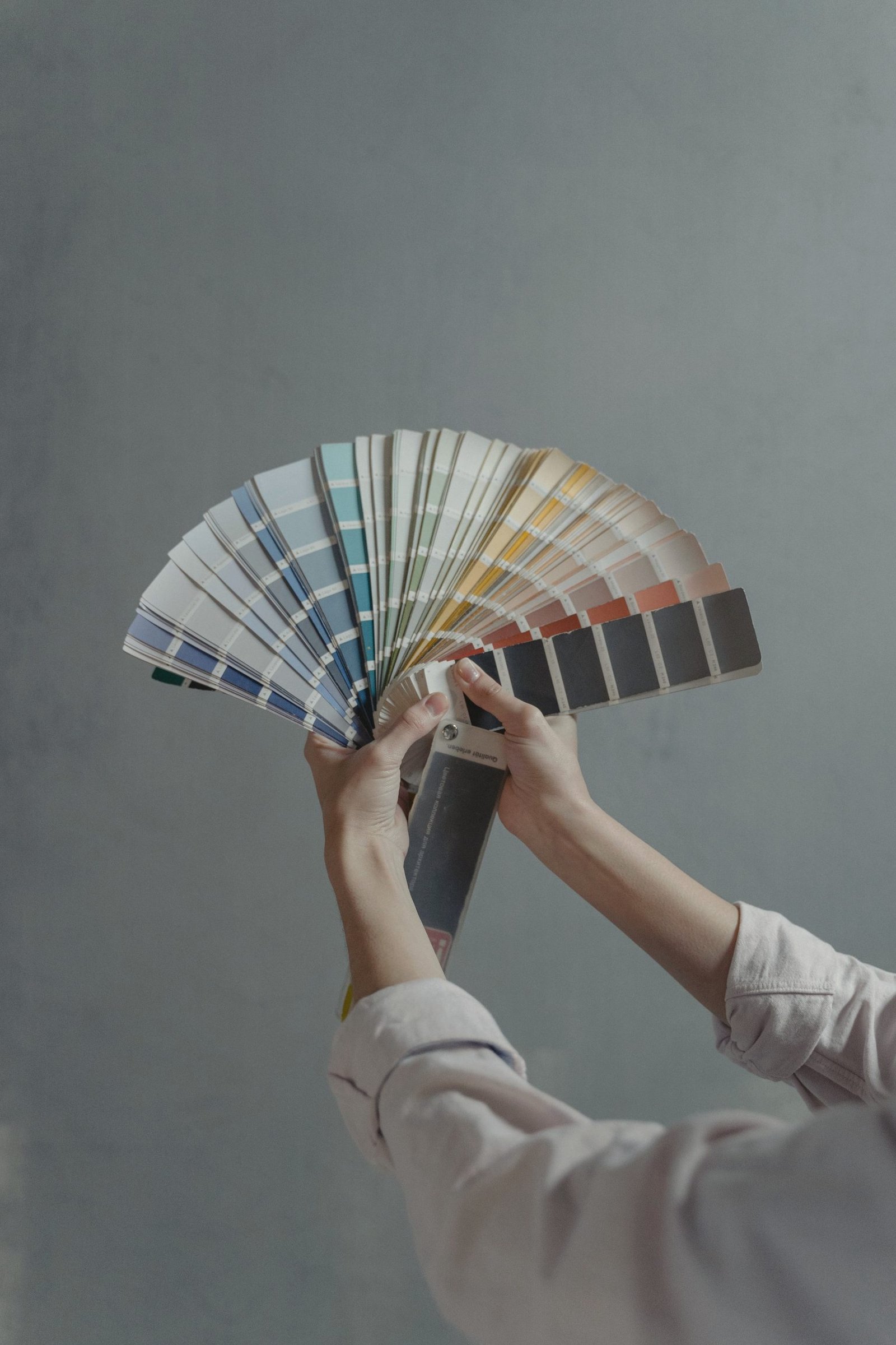 Hands holding a fanned deck of colour sample chips against a grey wall