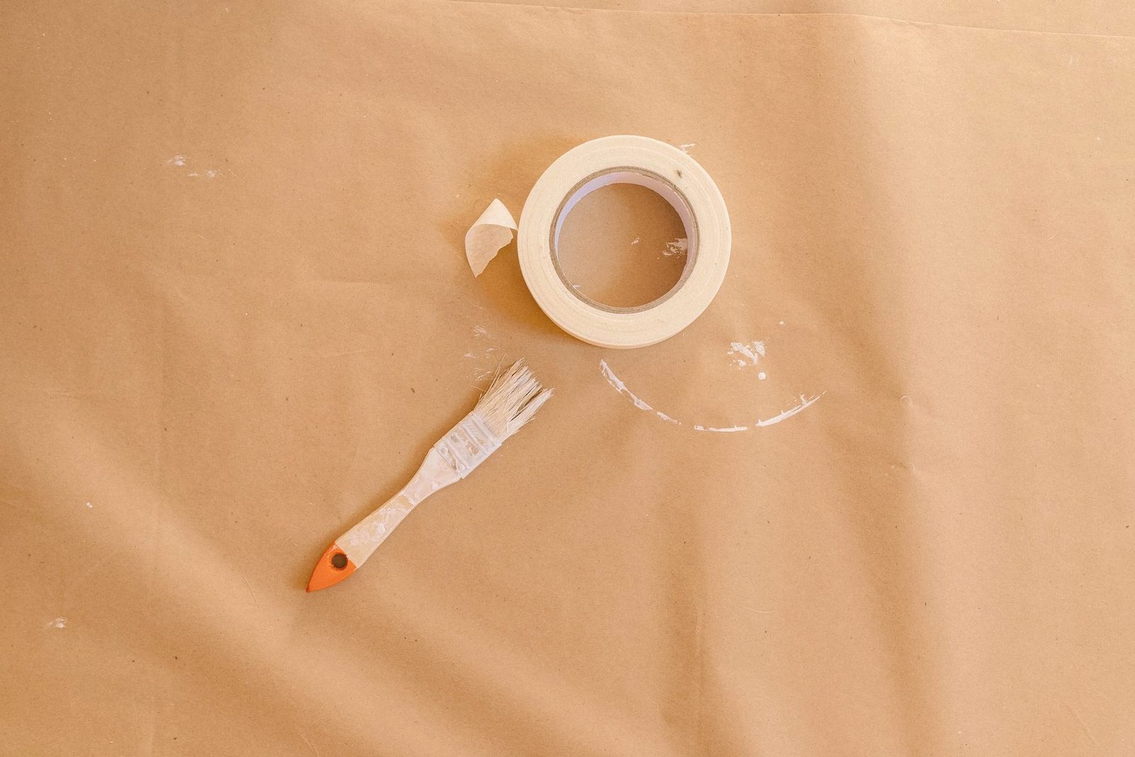 A roll of masking tape and a small brush lying on tan masking paper
