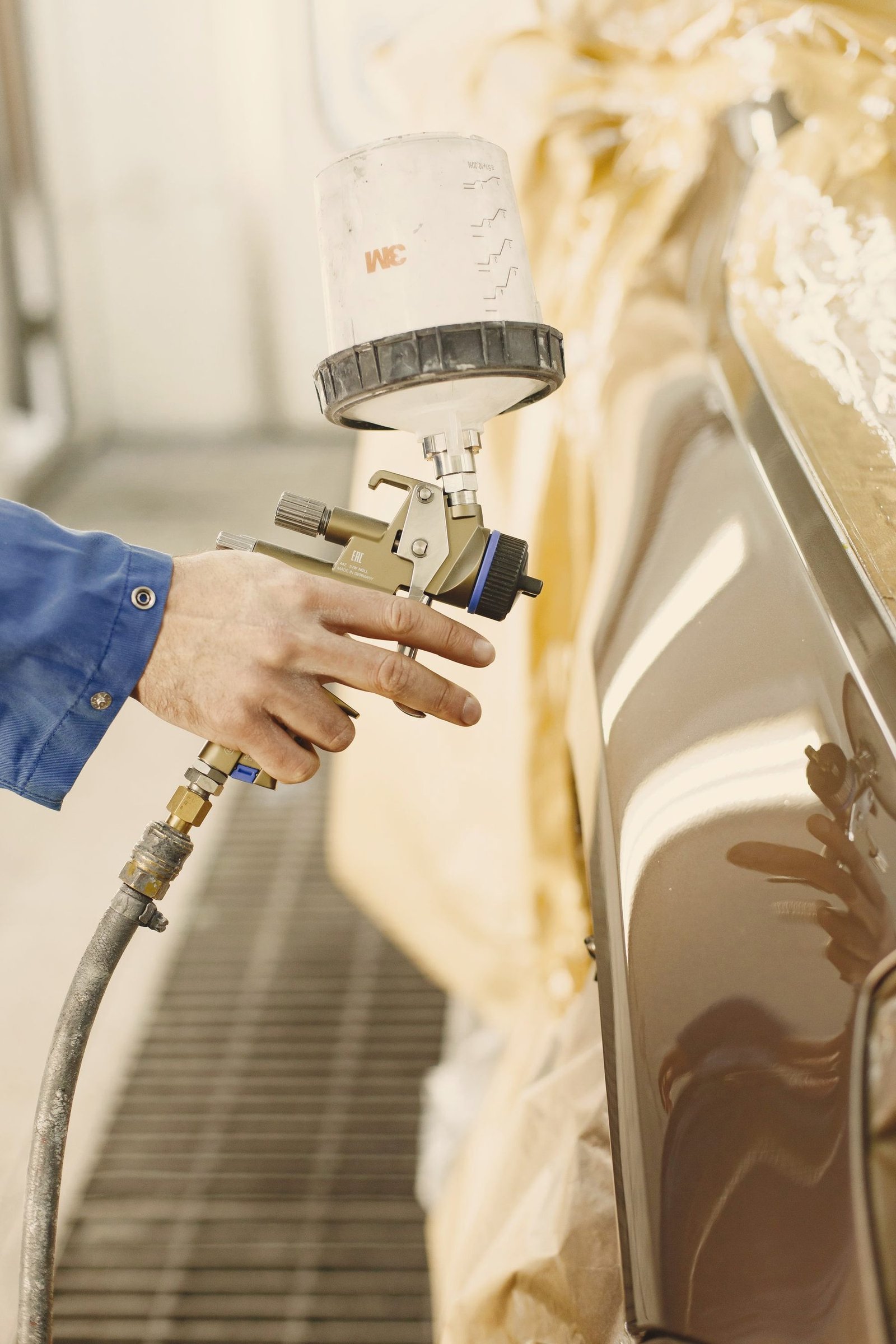 A gloved hand spraying gold paint along a car body with a gravity-feed gun